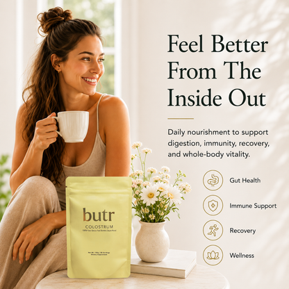 Woman holding a mug with 'butr' colostrum package and flowers on a table.